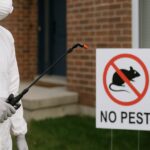 A professional pest control technician in protective gear spraying the exterior of a Toronto brick house.